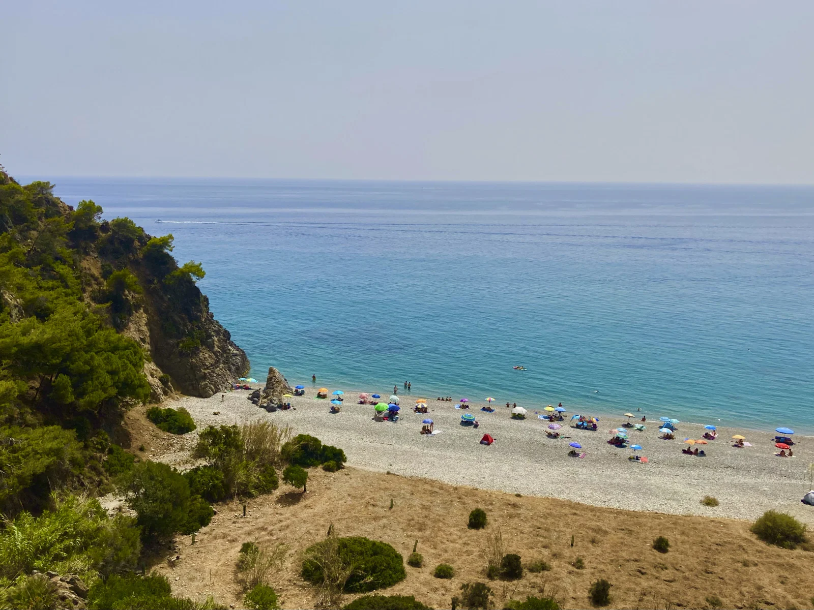 A beach at Nerja lies under a cliff, with umbrellas along the shore and the Mediterranean beyond.