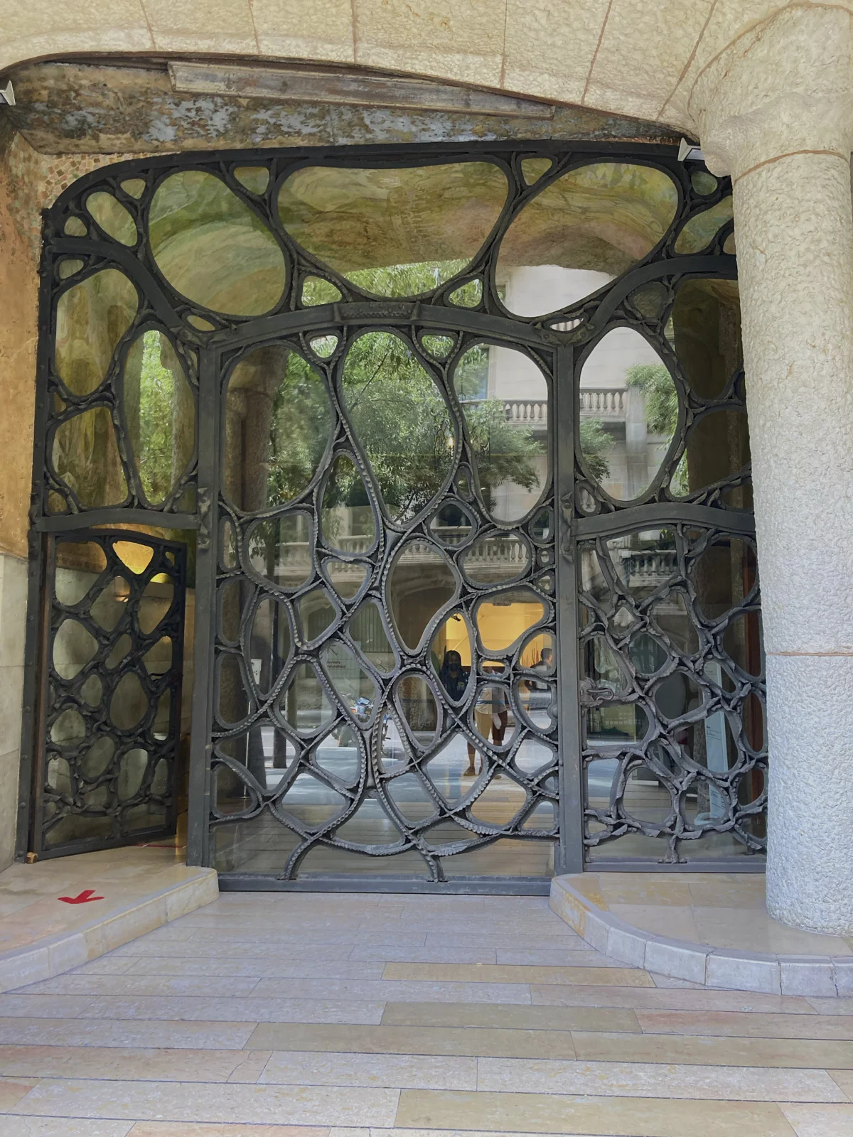 The organic iron gate at the entrance of La Pedrera in Barcelona stands between stone piers.