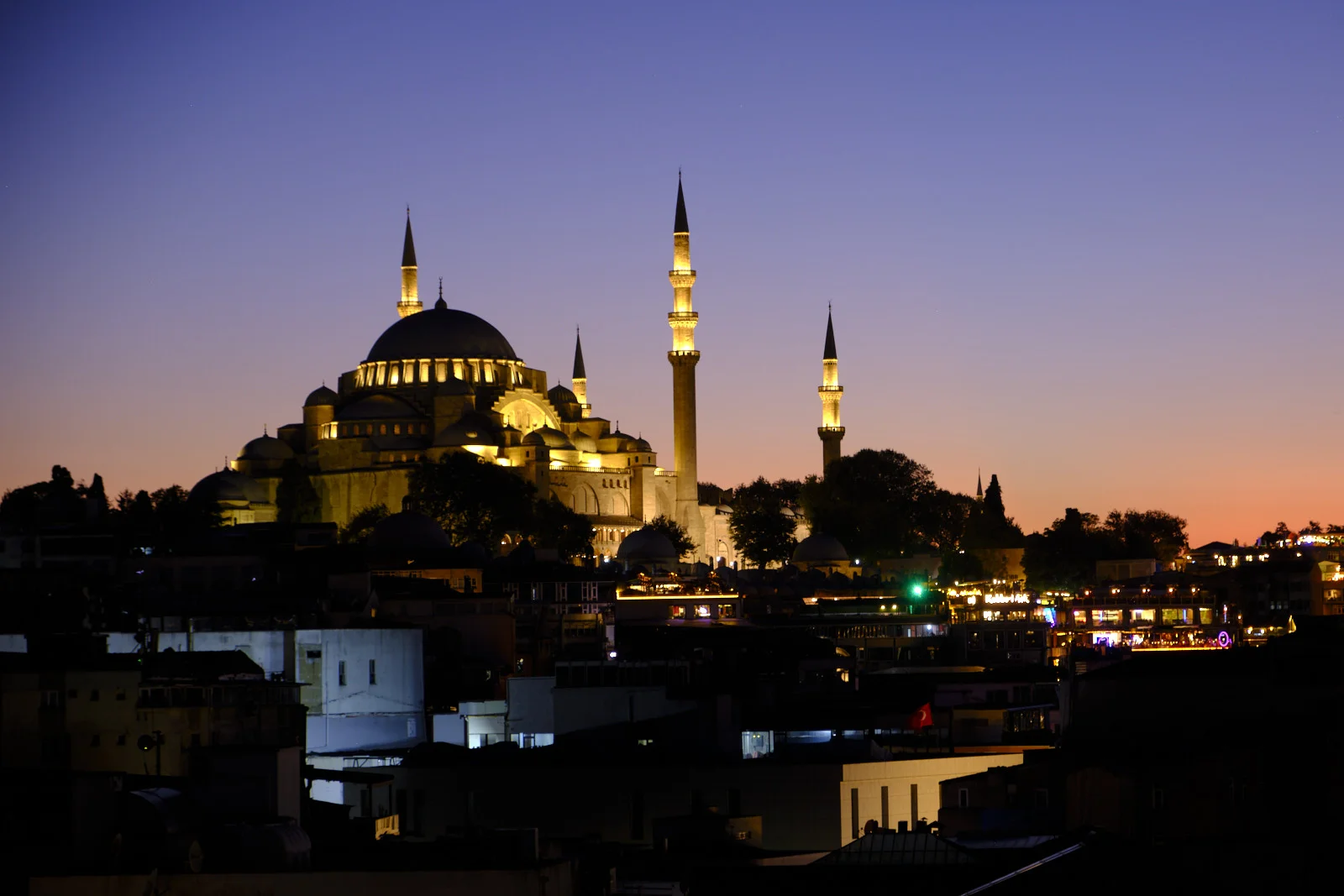 The floodlit Blue Mosque above dark city rooftops at dusk, with several minarets and a band of lights along the roofs below.