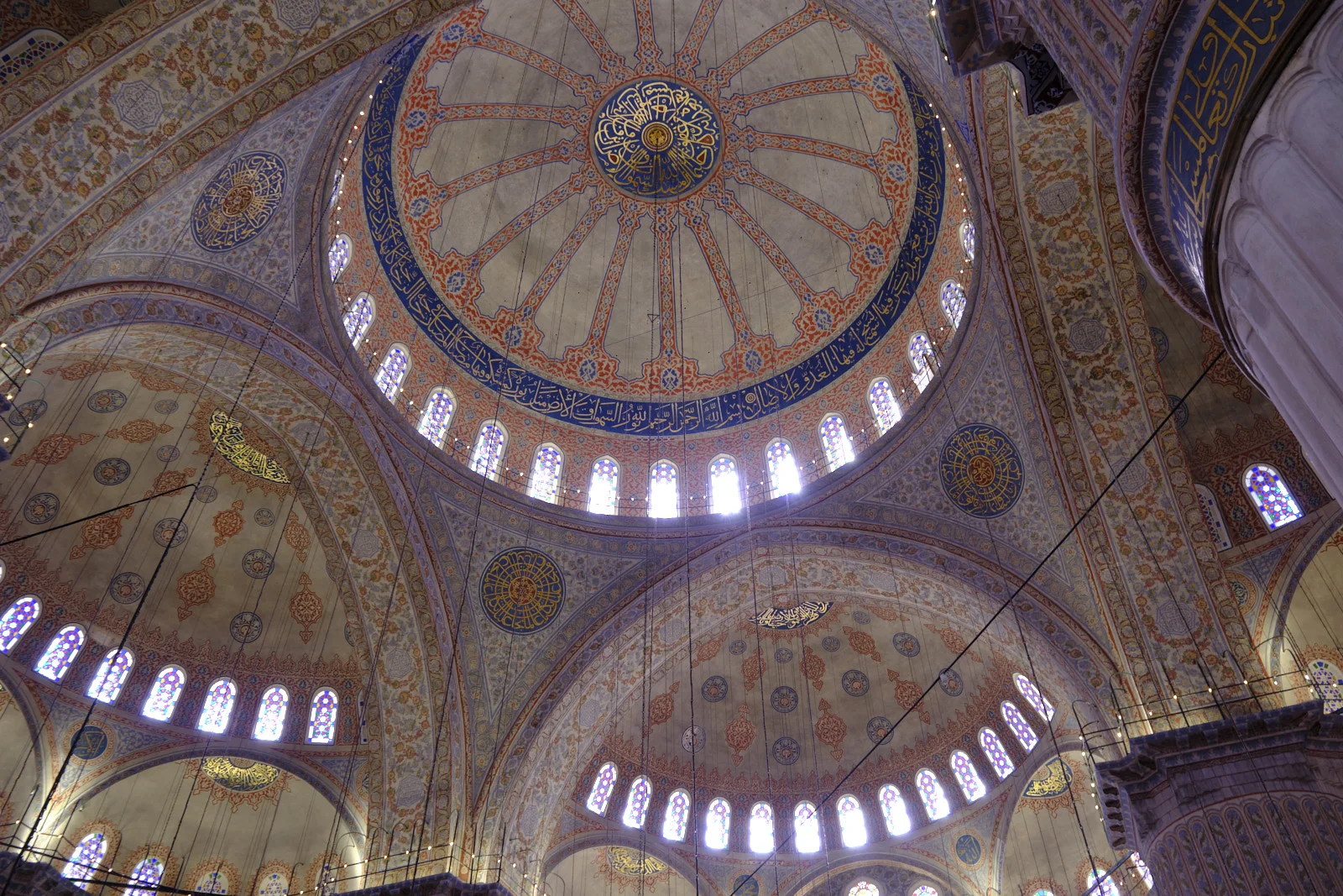 Looking up at the Blue Mosque's painted central dome, ringed by windows and smaller decorated domes.