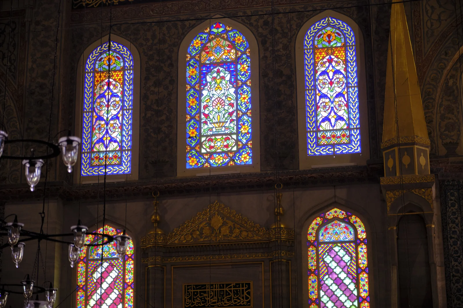 Tall floral stained-glass windows above a gilded niche and smaller colored windows in the Blue Mosque.