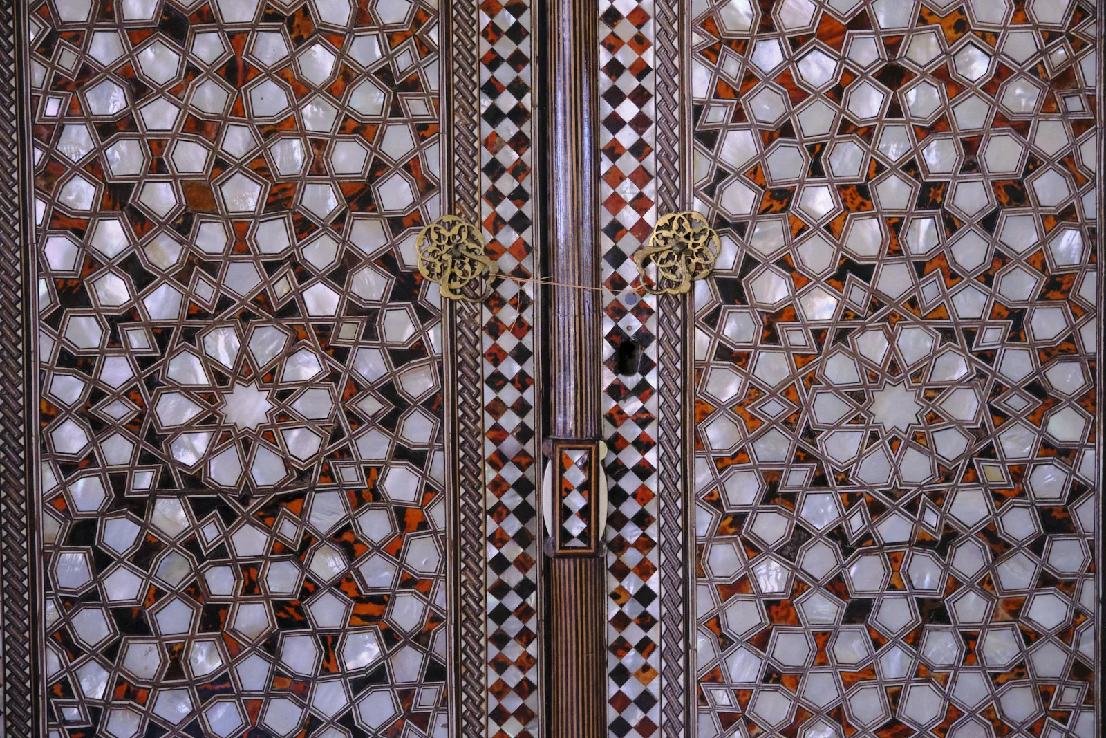 Close view of wooden doors inlaid with mother-of-pearl geometric stars and amber shell, with brass ring pulls.