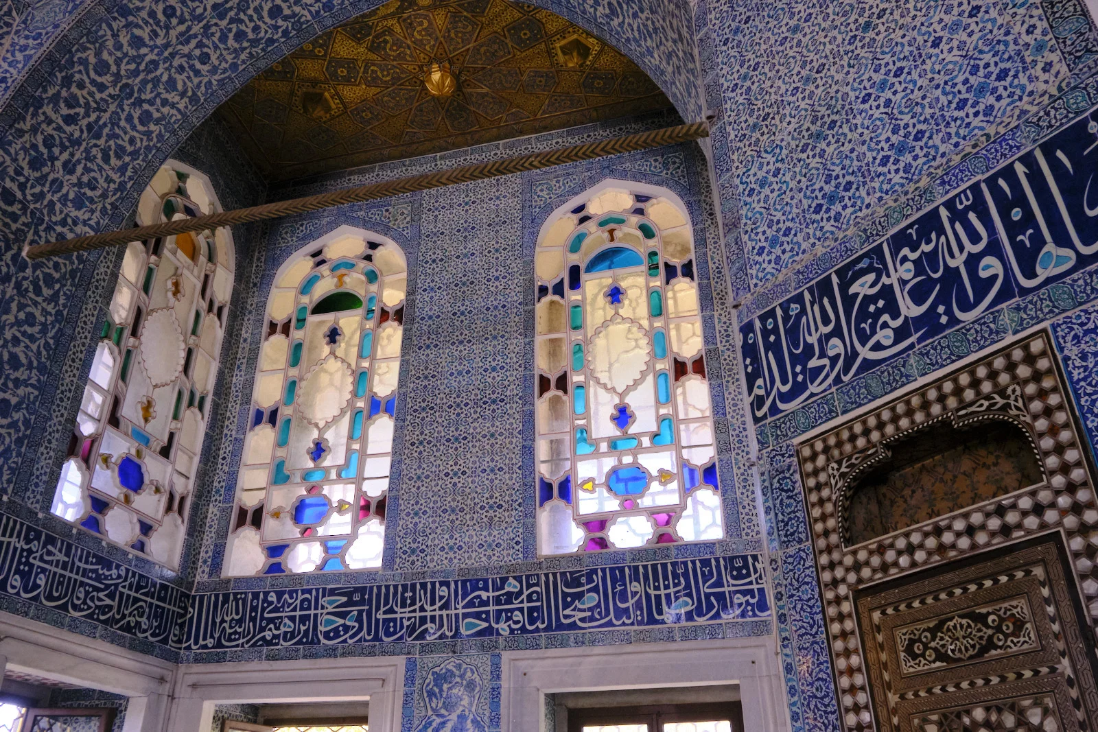 A room lined with blue-and-white tiles and calligraphy, with colored-glass windows and a gilded ceiling.
