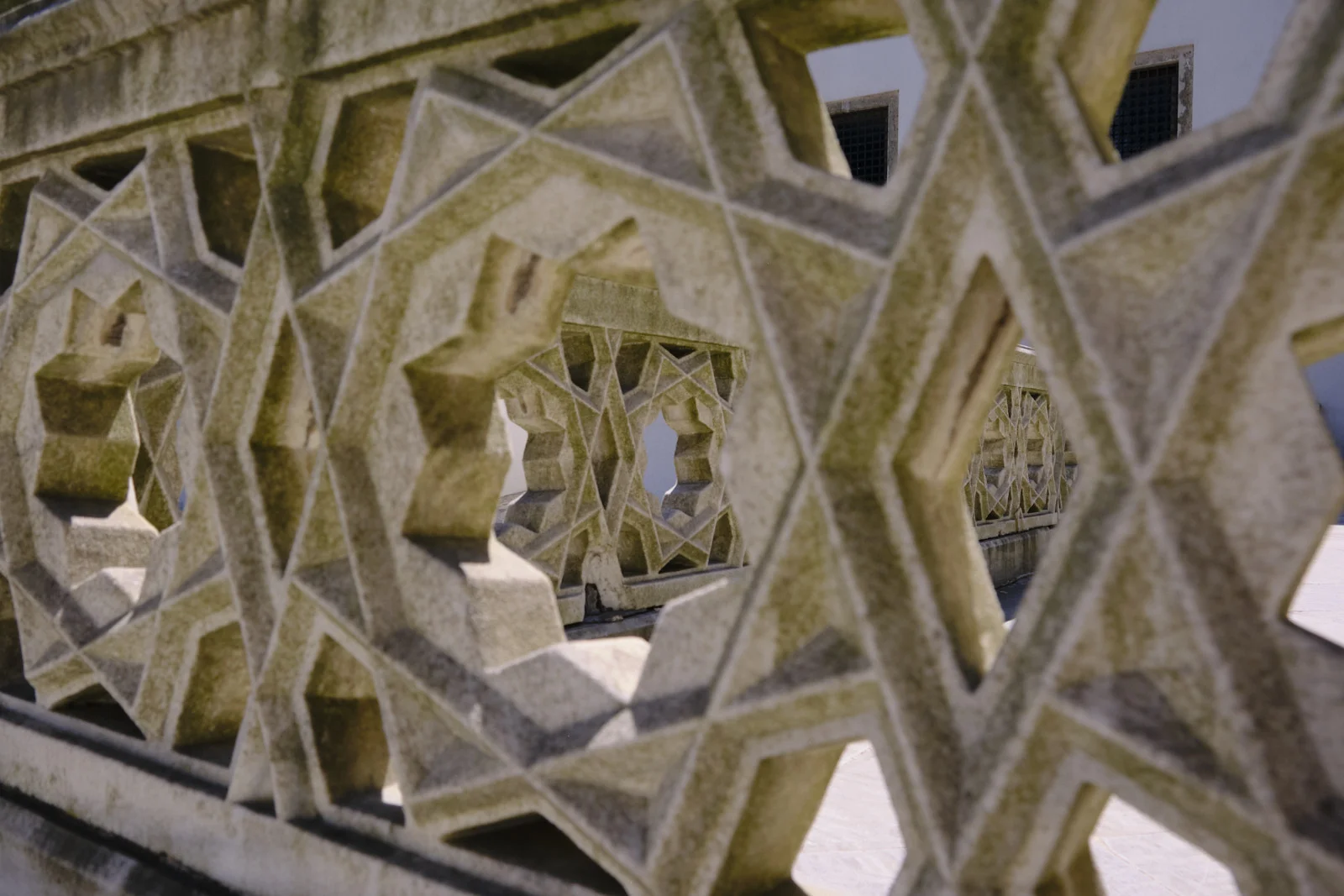 Close view of a thick geometric stone screen with star-shaped openings, and a second screen visible through them.