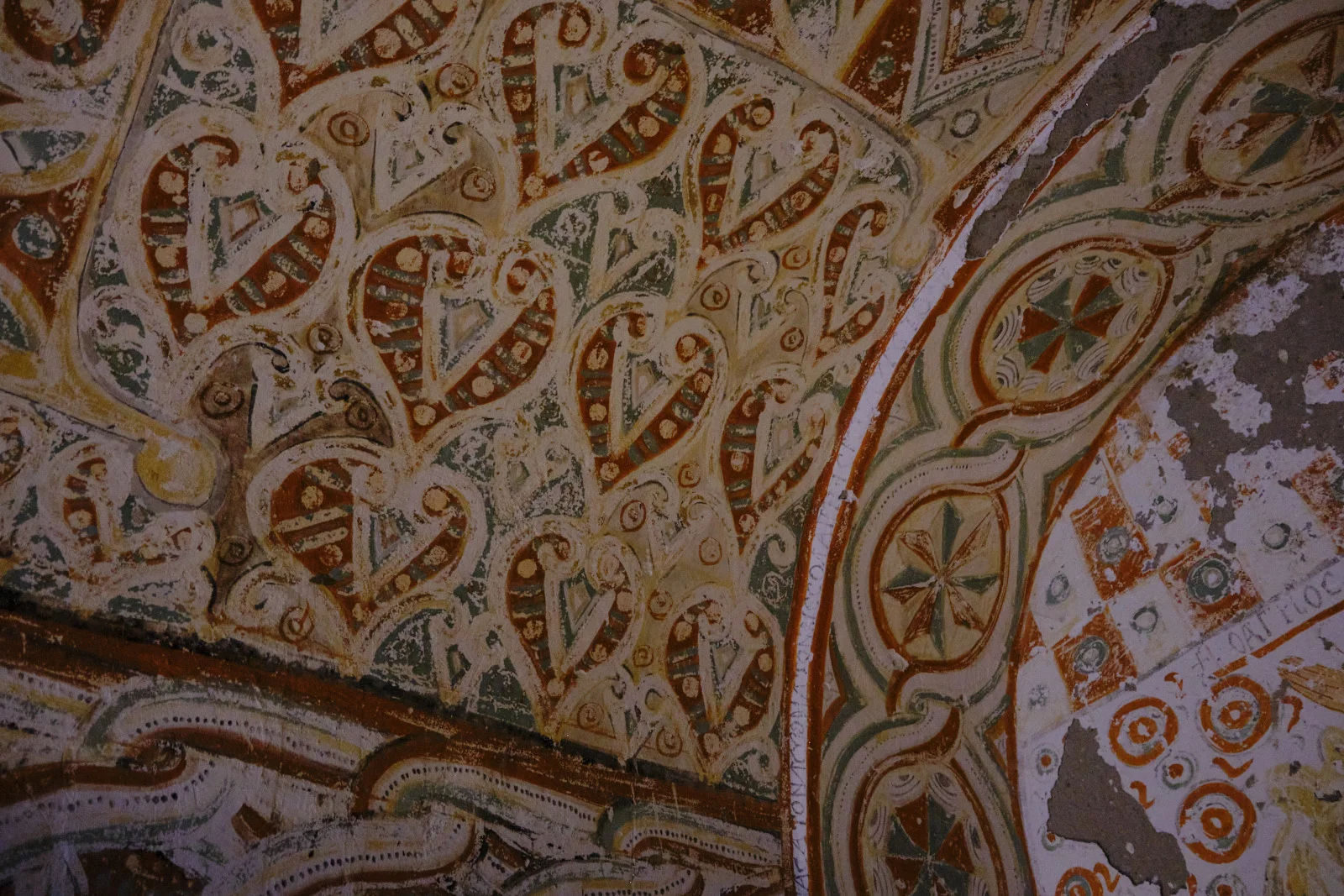 A close view of a worn church ceiling painted with interlocking heart-shaped motifs in rust and green, plus circular crosses along a curved arch.