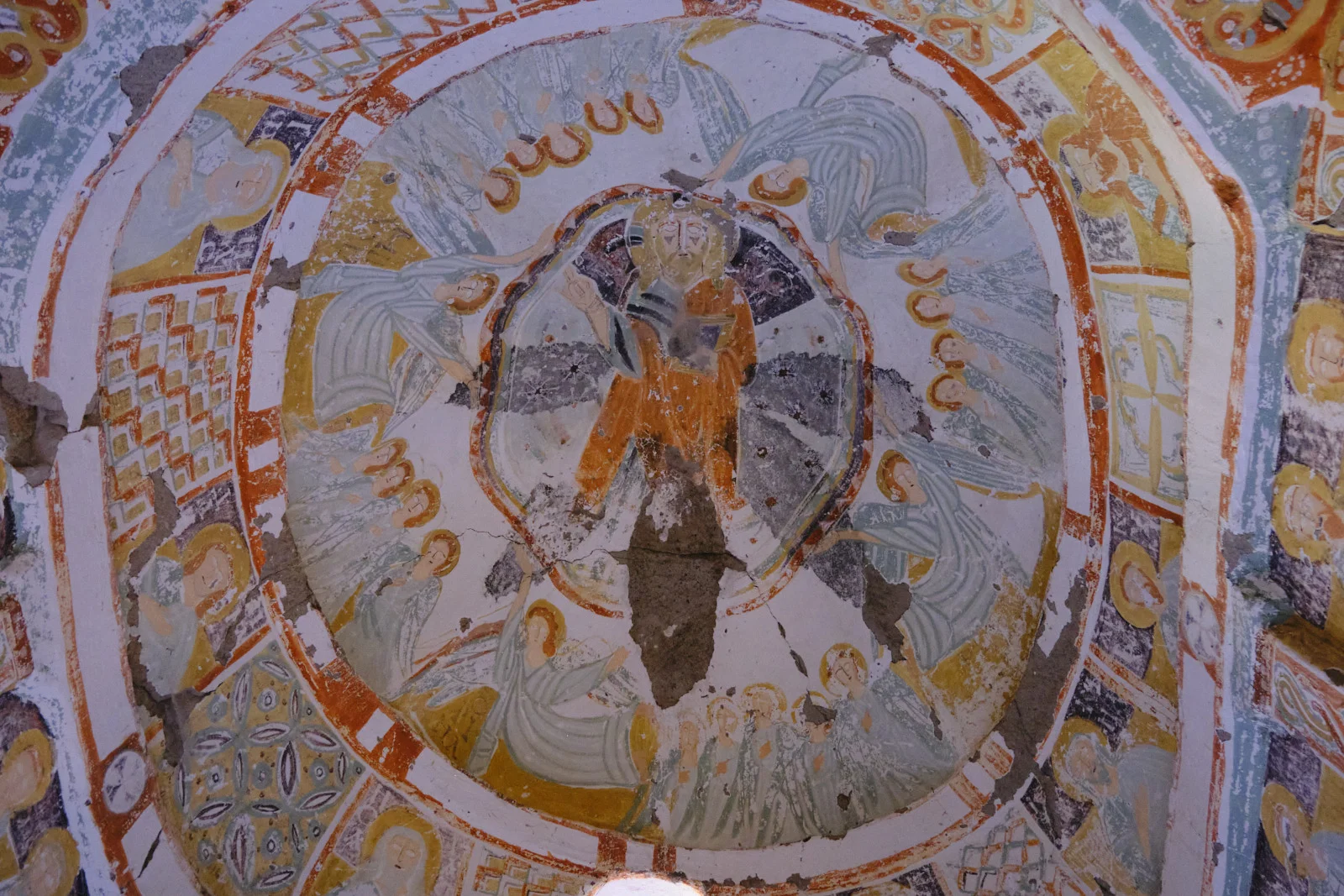A damaged dome fresco shows Christ in orange at the center, surrounded by haloed angels in pale robes, with geometric borders and a large area of lost plaster.