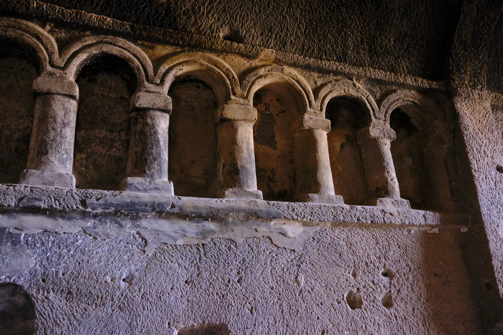 A carved stone arcade of columns and arches above a rough, pitted plaster wall inside a rock-cut interior.