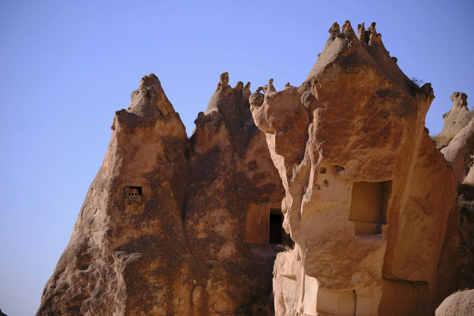 Sunlit reddish rock towers with jagged crests, a small square window on the left, and a larger rectangular opening on the right.
