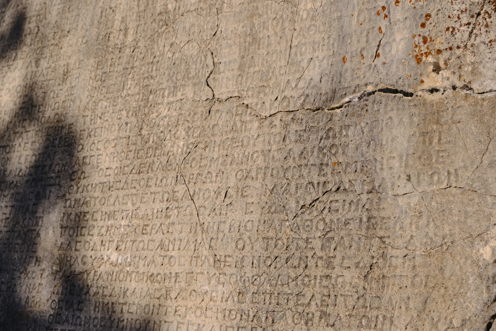Close view of an ancient Greek inscription carved into cracked, lichen-speckled stone.