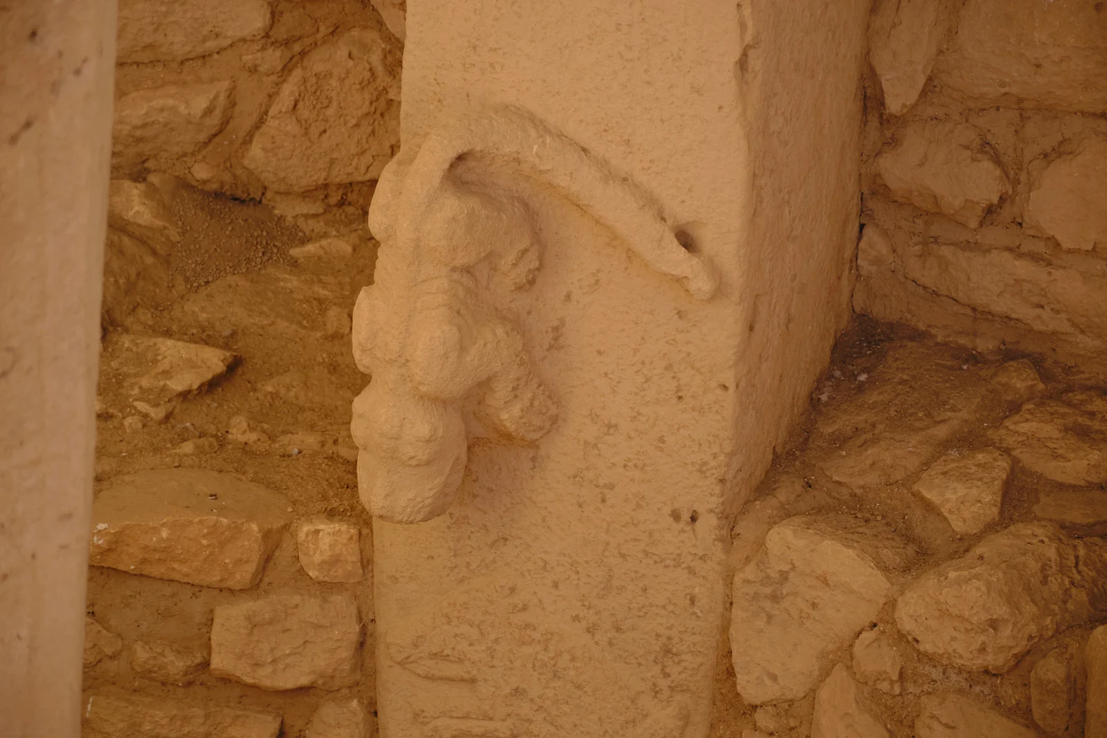 A high-relief animal carving projects from the edge of a limestone pillar against a rough stone wall.