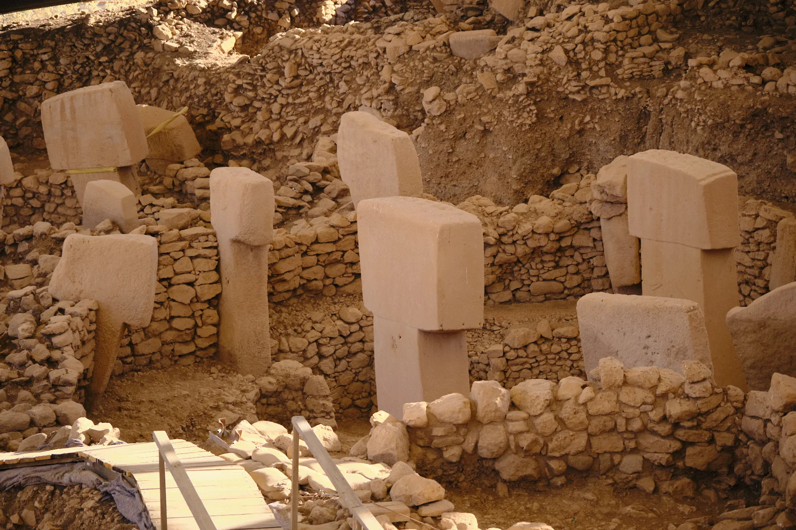 Several T-shaped limestone pillars stand in a circular stone enclosure above a wooden walkway.