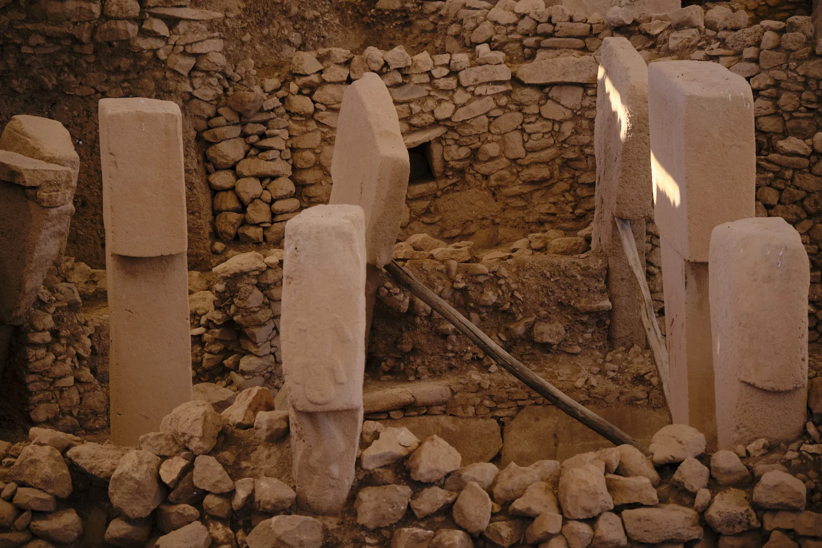 Leaning T-shaped pillars in a stone enclosure are propped with wooden beams above a pile of loose rocks.