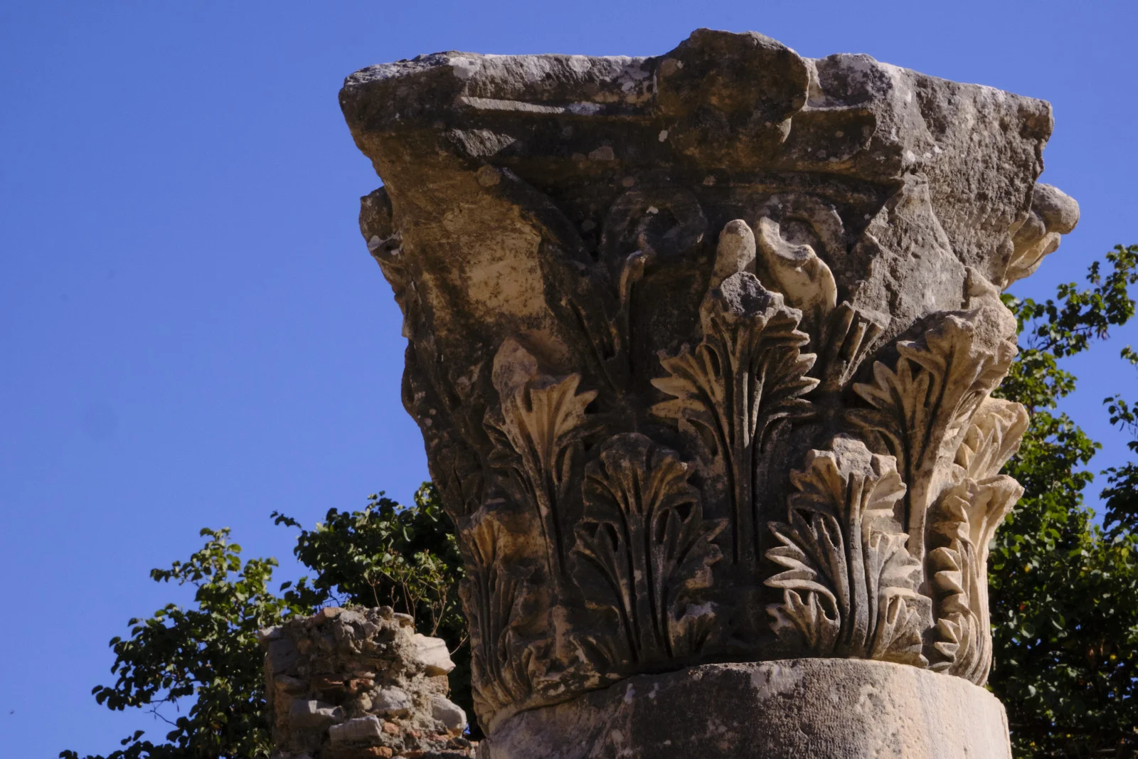 Close view of a carved Corinthian column capital with layered acanthus leaves against a clear blue sky.