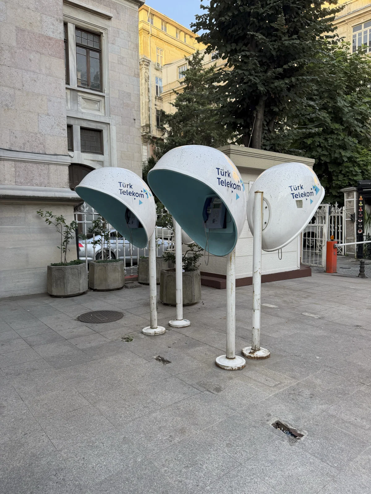 Three white mushroom-shaped Türk Telekom phone booths with turquoise undersides on a stone sidewalk.
