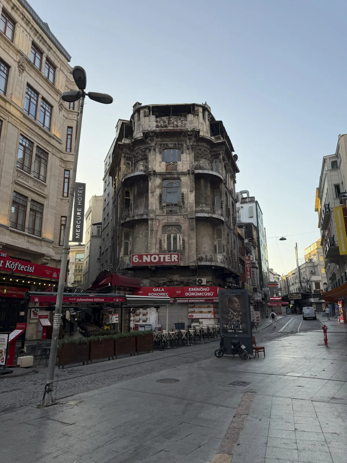 A fire-blackened ornate corner building with a red 6. Noter sign, above street shops and a Mercure Hotel blade sign.